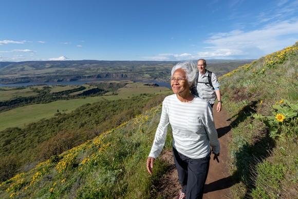 An older couple smiling as they hike along a beautiful hillside. 
