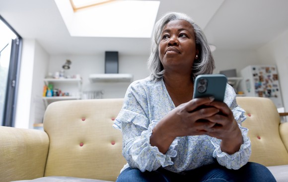A person sits on their couch while holding a smartphone.