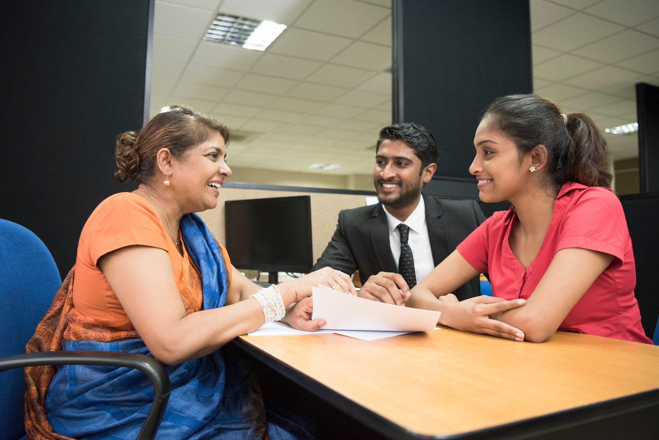 Three investors sit around a table and review some papers in an office room.