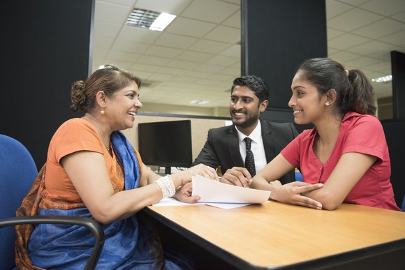 Three investors sit around a table and review some papers in an office room.