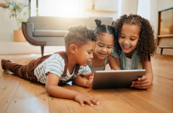 Three people lying on the floor, collaboratively using a mobile computing device.