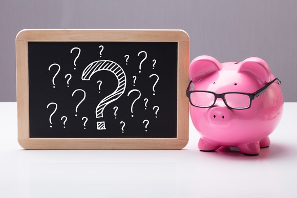 Piggy bank beside a chalkboard with question marks.
