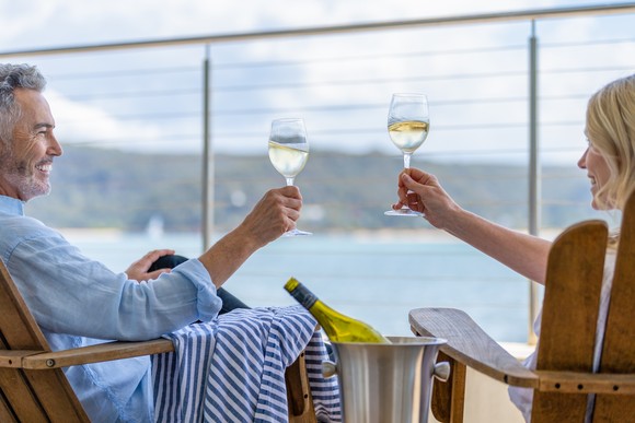 A couple making a toast while sitting on an outdoor cruise ship deck.