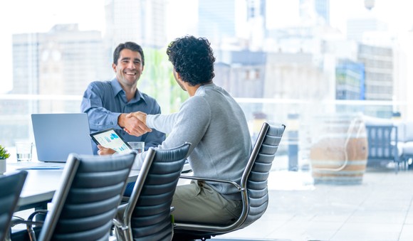 Two people in an office shaking hands after agreeing to a financial arrangement. 