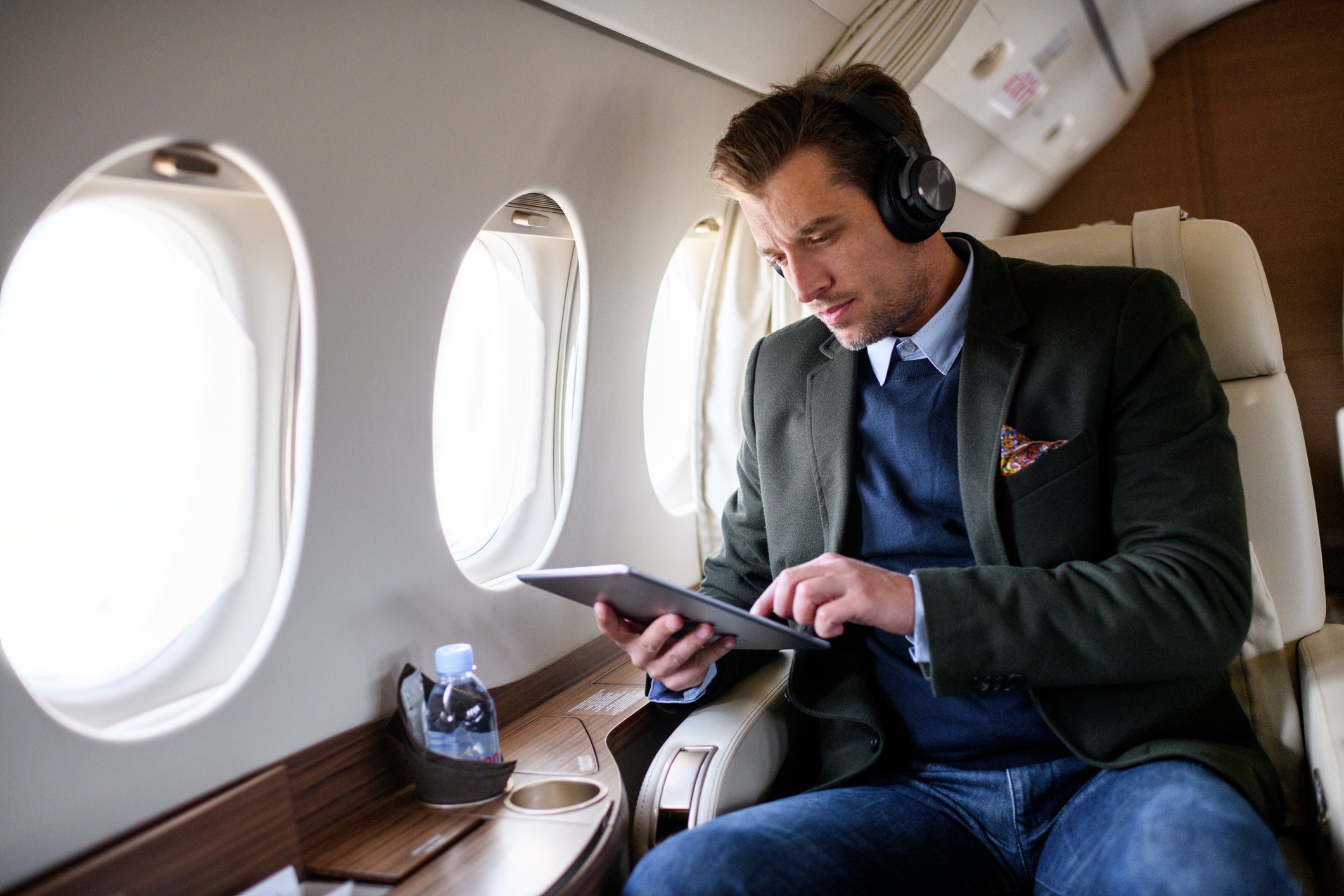 A wealthy person sits on a private jet and studies his digital tablet.