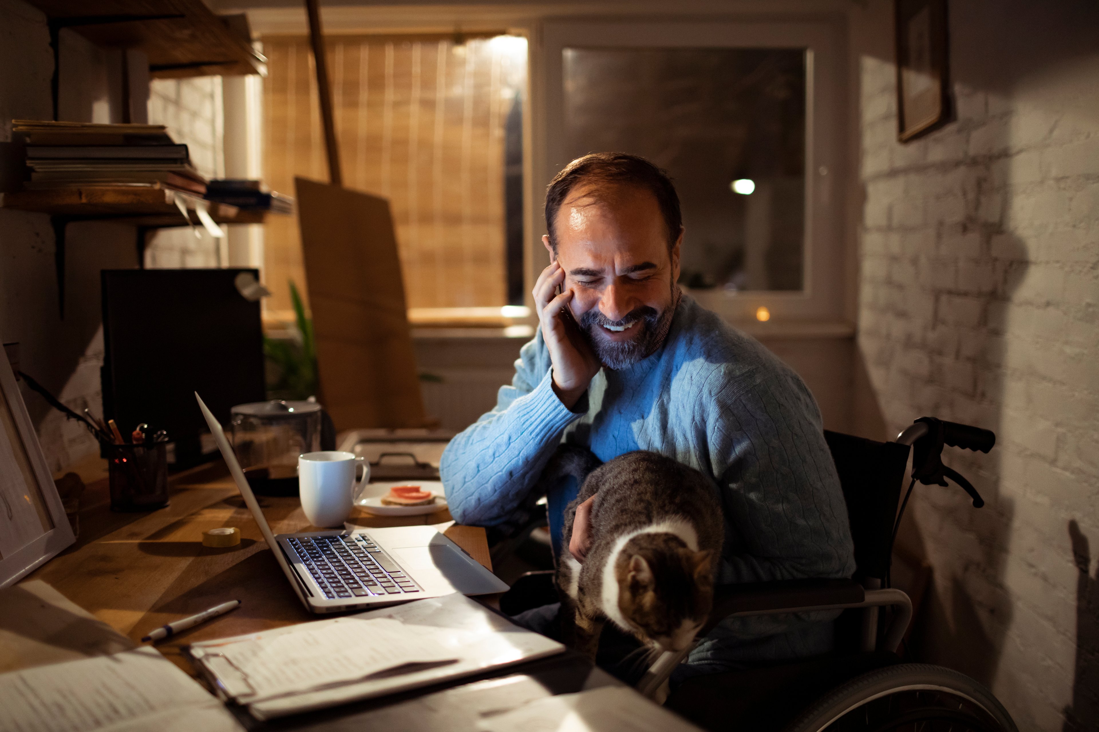 A person sits at a desk while holding a cat.