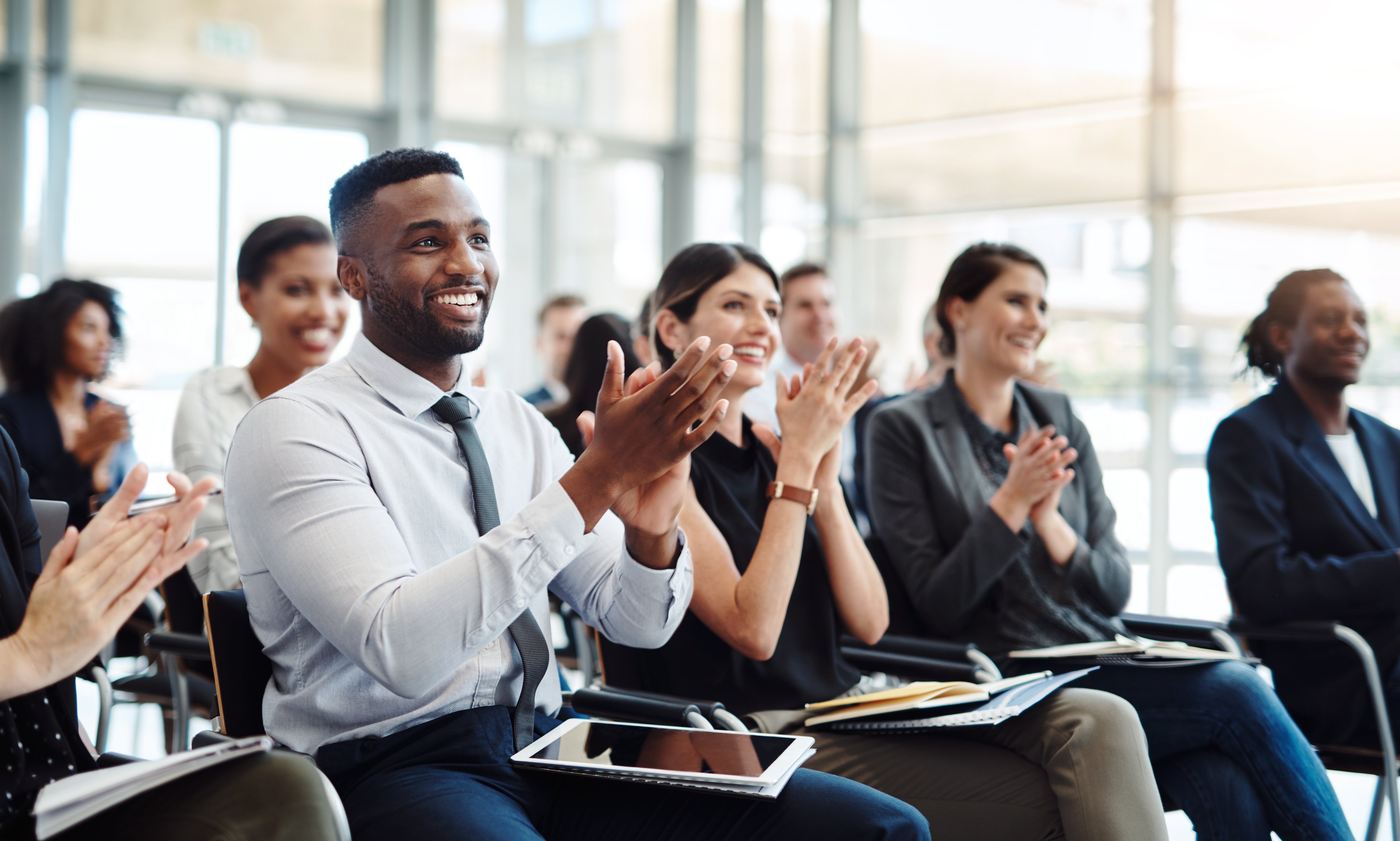 A group of ipeople applaud while sitting in an office conference room.