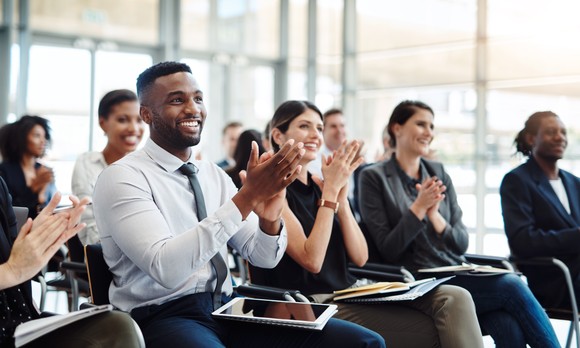 A group of ipeople applaud while sitting in an office conference room.
