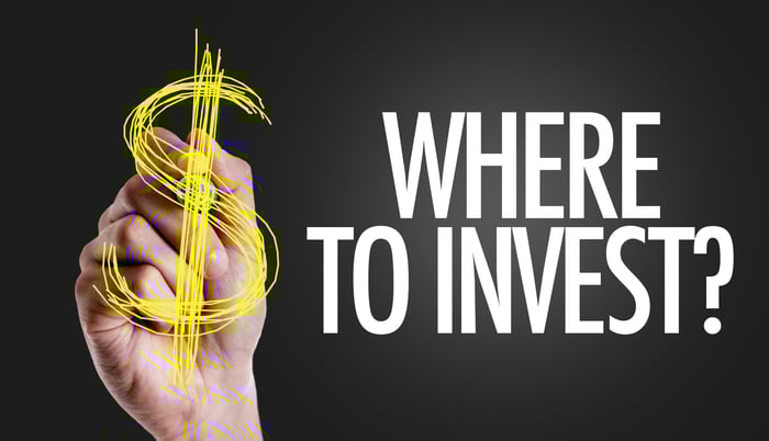 Someone drawing a dollar sign on a signboard that asks where to invest.