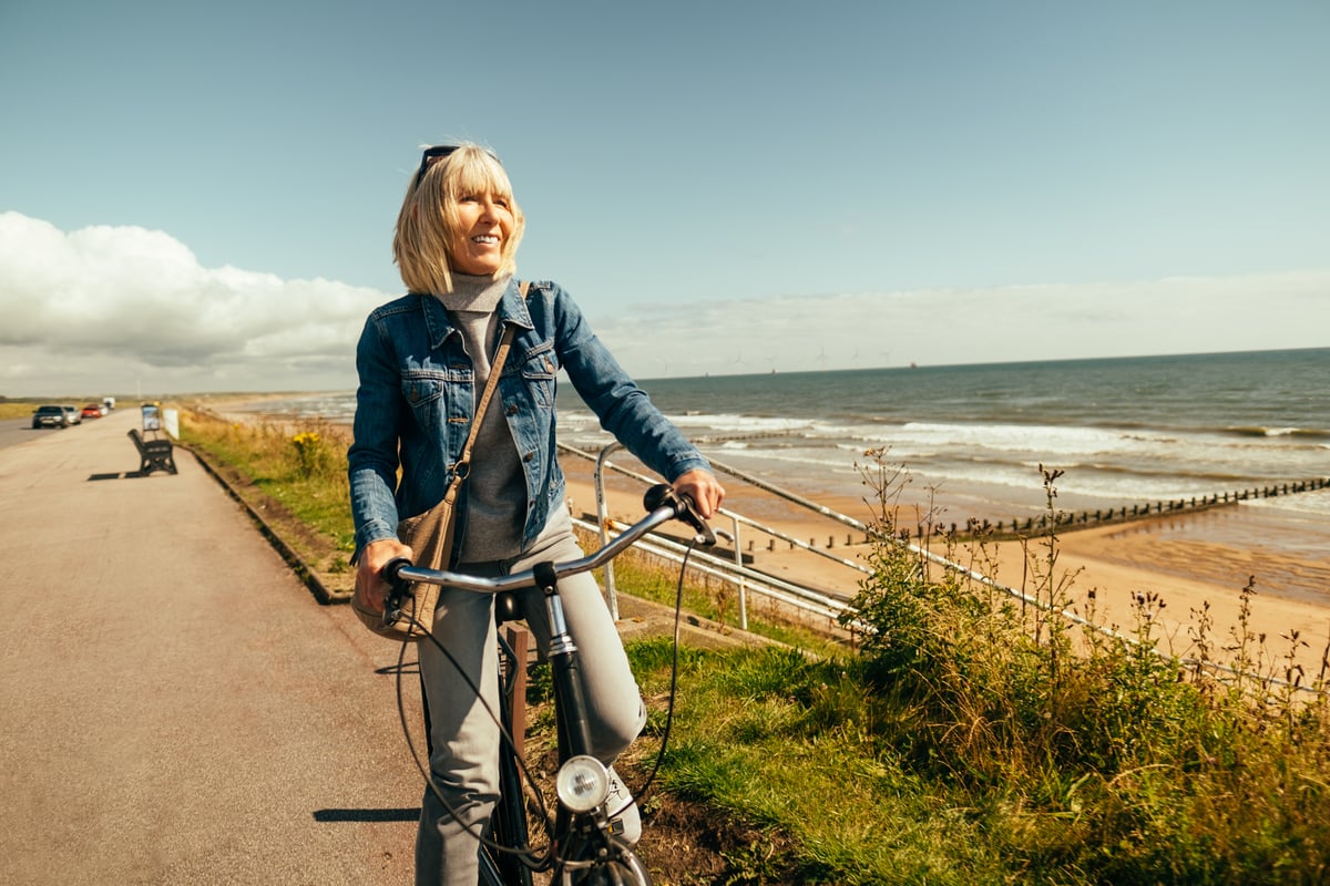 A smiling person riding a bike by the ocean.