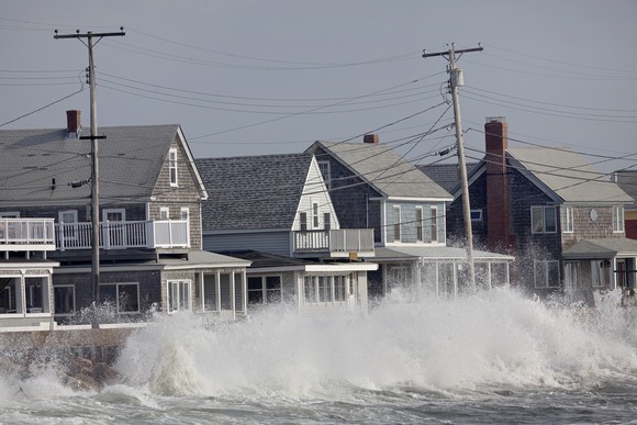 Waves crash onto beach with homes close to the water. 