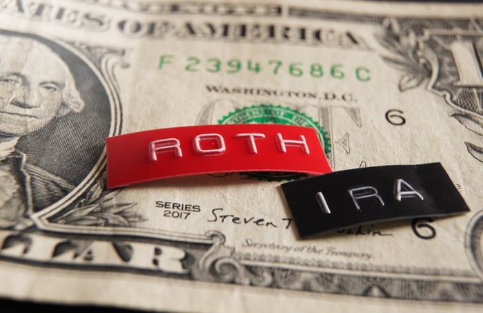 A dollar bill with a red and black label on top. The labels read "Roth IRA."