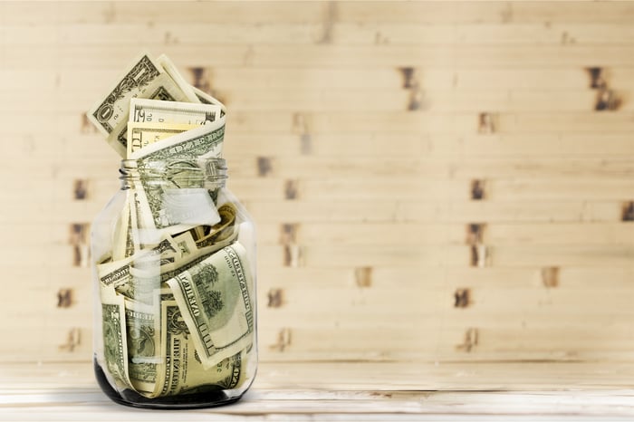 A glass jar full of different denominations in bills on a wooden table.