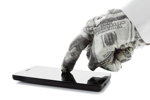 Hand wrappe in $100 bills tapping a cellphone.