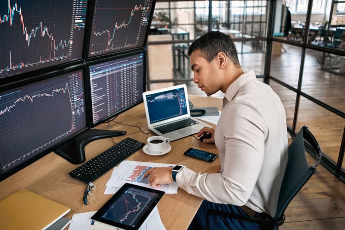A trader sitting in front of several computer monitors displaying stock charts.