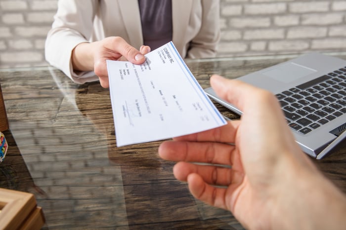 A hand passing a check payment to another hand.