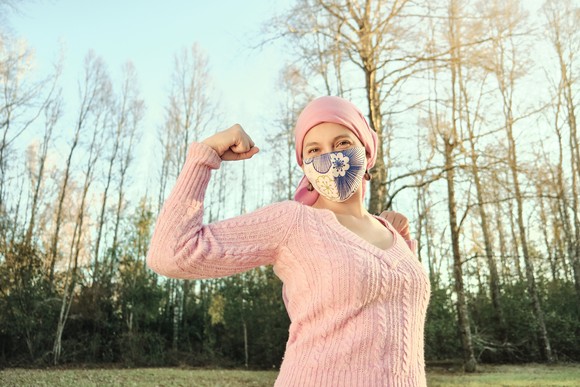 A person wearing a face mask flexes their bicep.