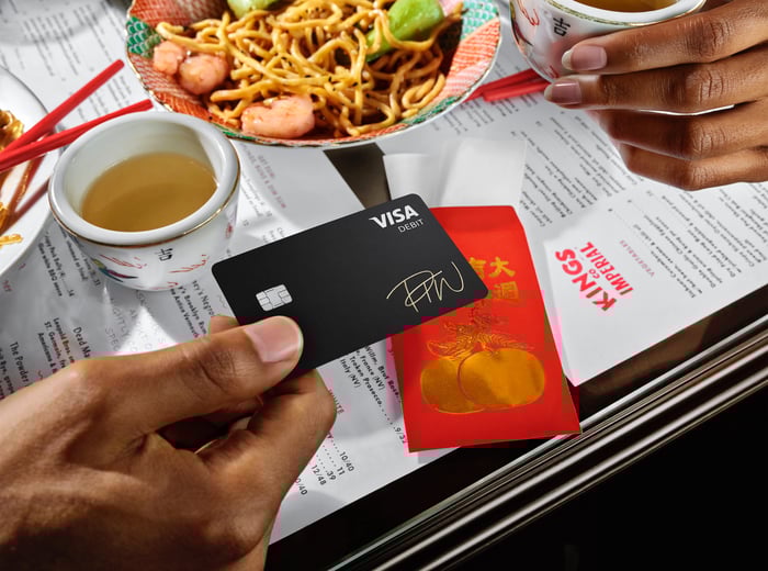 Hand holding a Visa card over a table with a menu and food on it.