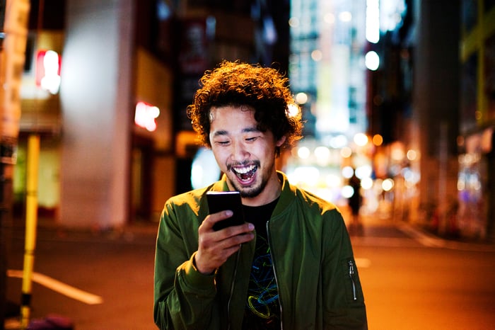 Smiling young person looking at phone on busy city street