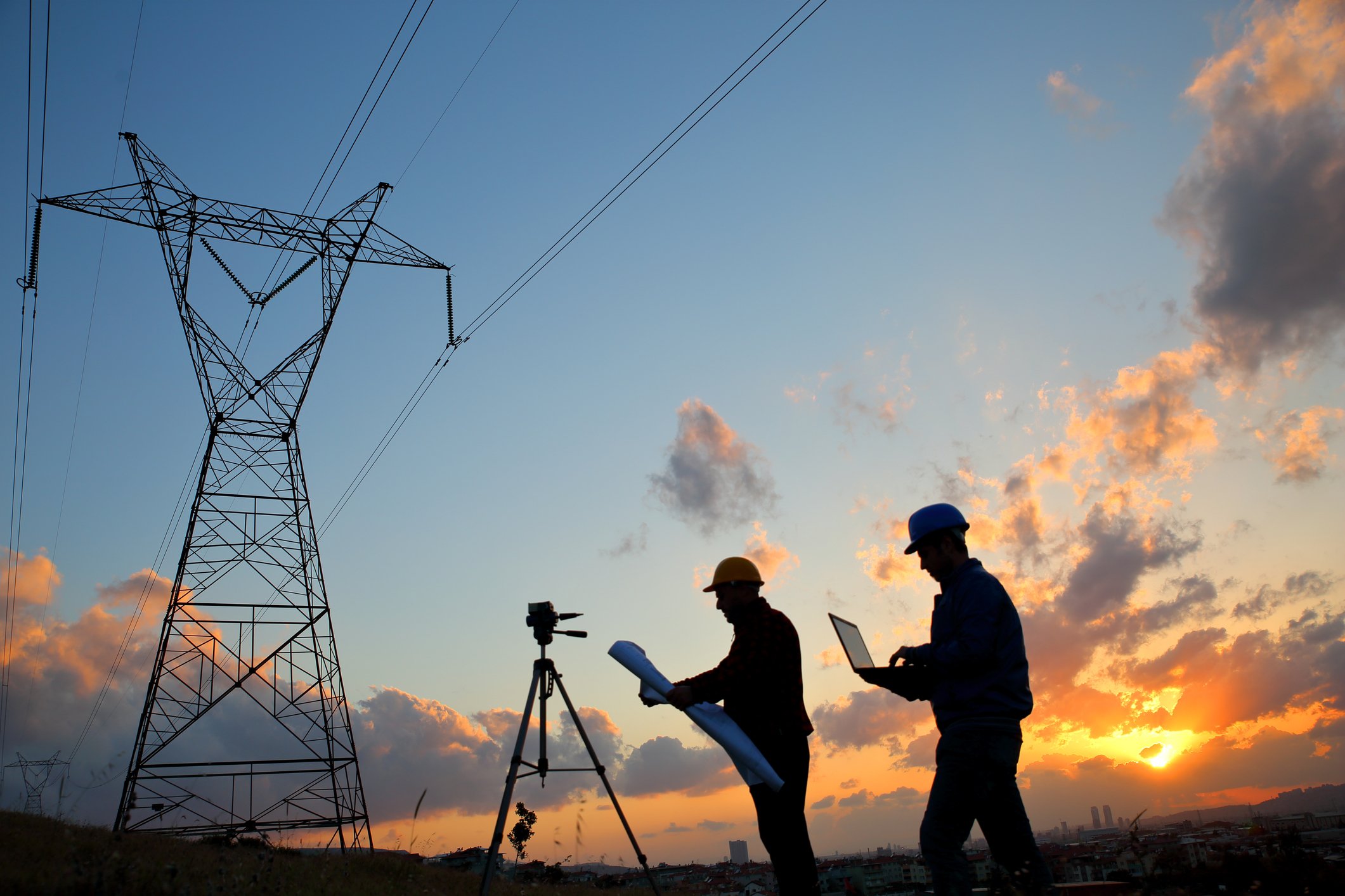 Silhouettes of two people standing underneath electric power lines.