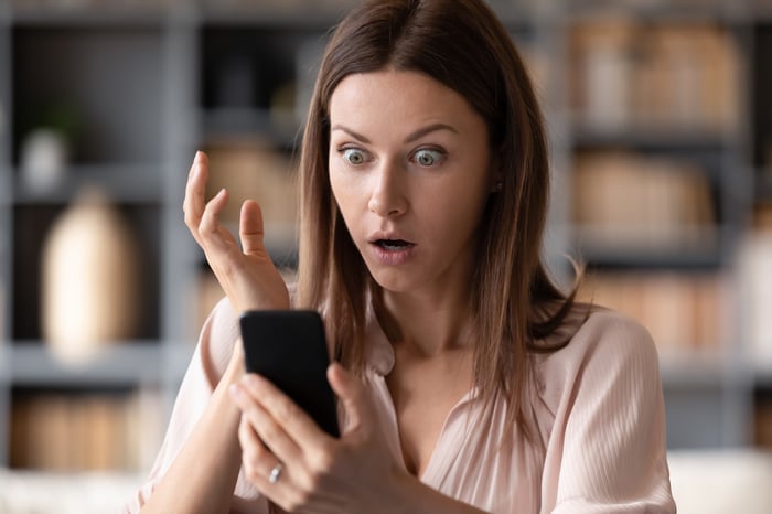 A person looks at a smartphone with a shocked look on their face.