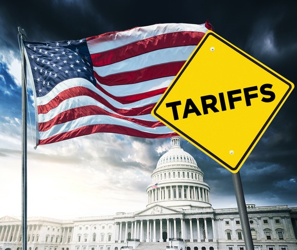 A yellow tariffs signboard with the American flag and Capitol building in the background.