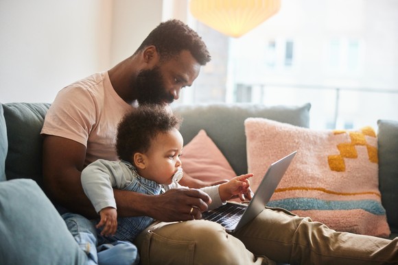 A person sitting on the couch and looking at a laptop with their child.