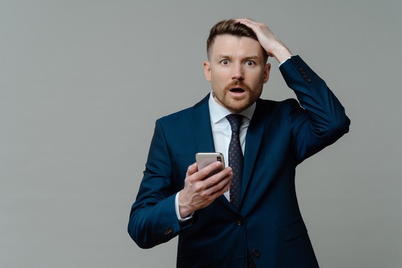 Shocked investor wearing a suit and holding a smartphone.