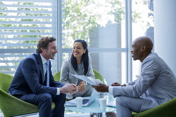 Three investors sit around a coffee table and discuss some papers in an office.
