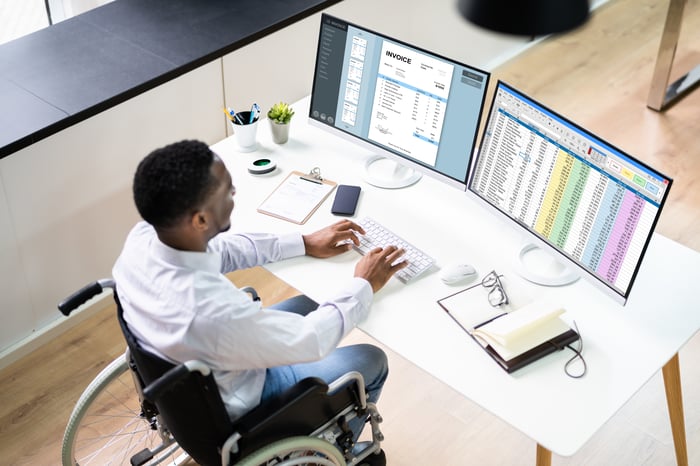 Person in wheelchair sitting in front of two monitors and typing.
