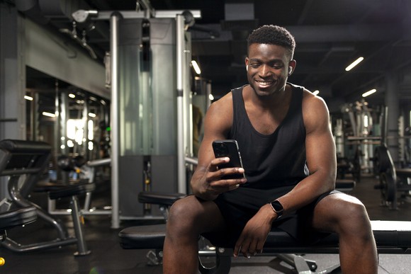 Person smiling and looking at a smartphone in a gym.