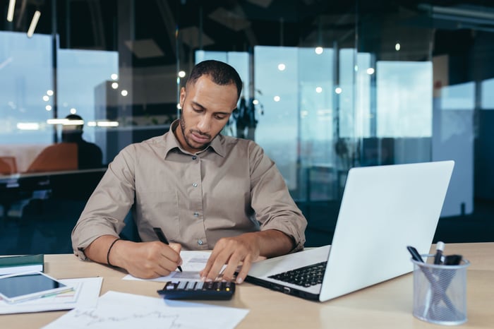 Person sitting in front of laptop while using a calculator. 