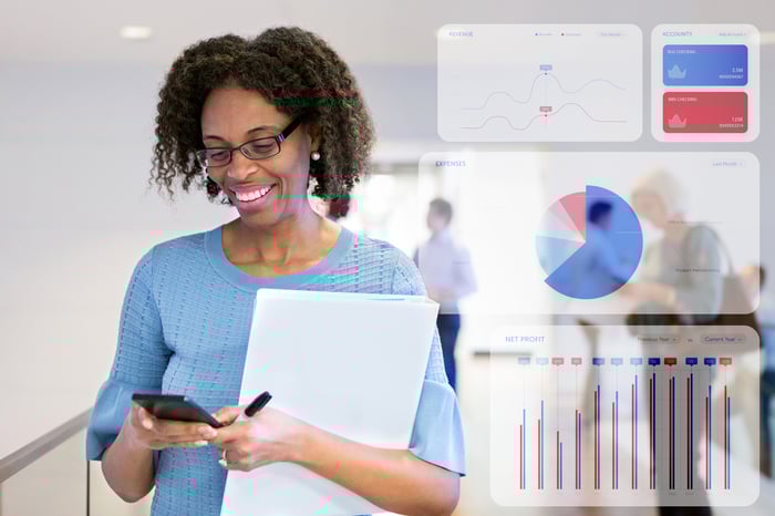 An investor is looking at a phone, with investment graphs in the background.