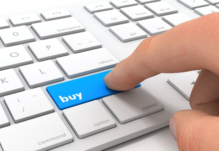 Person pressing a button marked as "buy" on a keyboard.