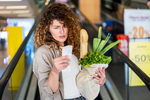 A person holding a bag of groceries and looking at their receipt.