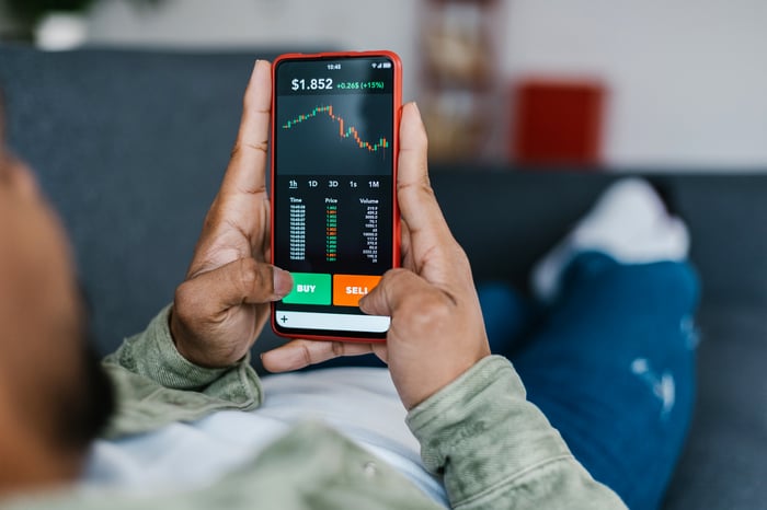 A person reviews a stock chart on their phone while laying on the couch.