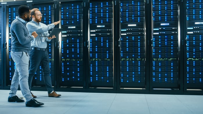 Two people walking through a data center pointing at server racks.