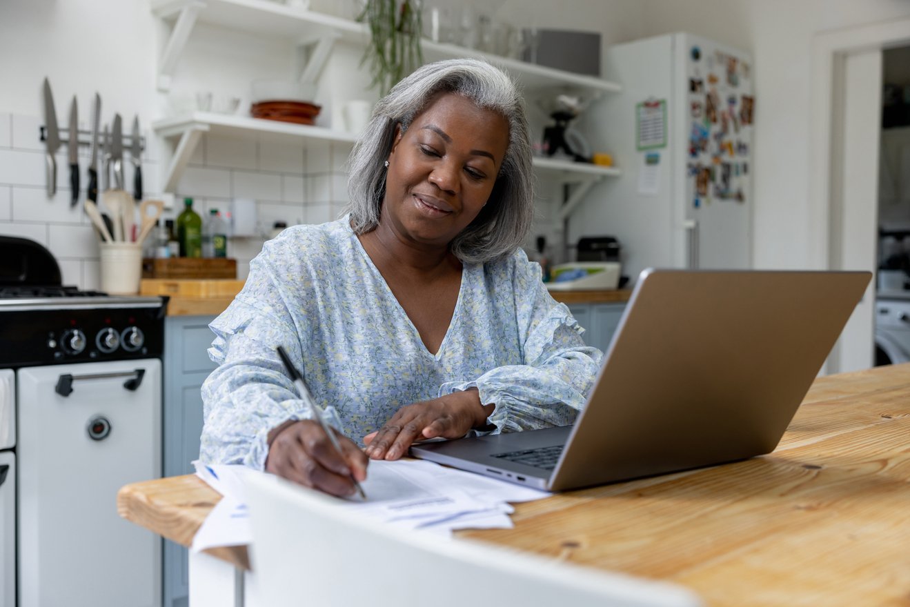 Smiling person writing note while sitting in front of laptop.