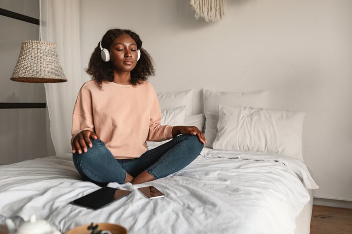 A person sitting cross-legged and listening to headphones.