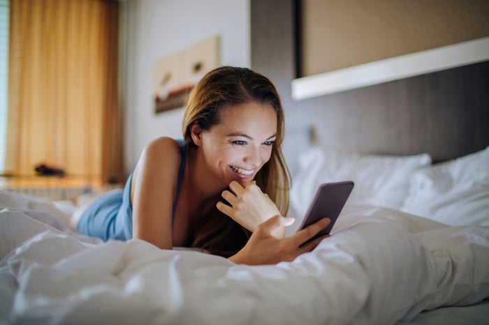 Person lying on a bed, looking at a phone. 