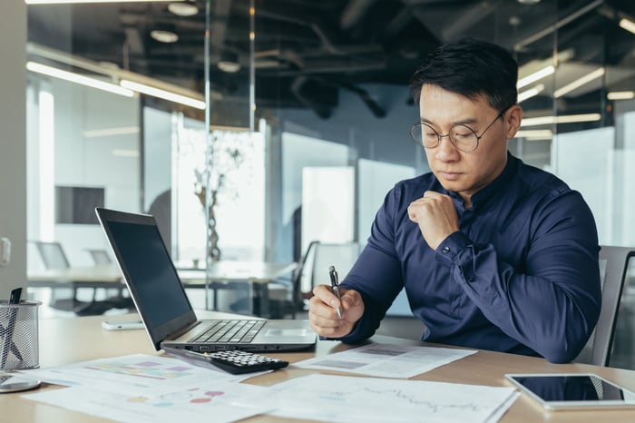 A person sitting at a desk reviewing paperwork in front of a laptop.