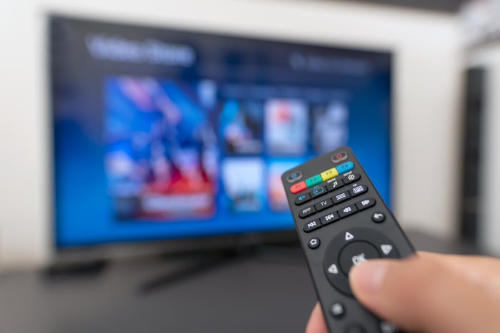 Hand holding remote in front of TV.