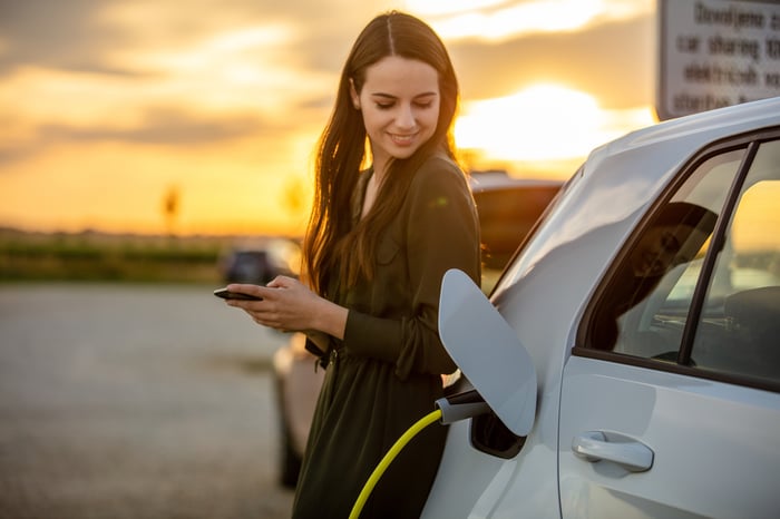 A woman smiles while looking at her electric vehicle that is charging. 