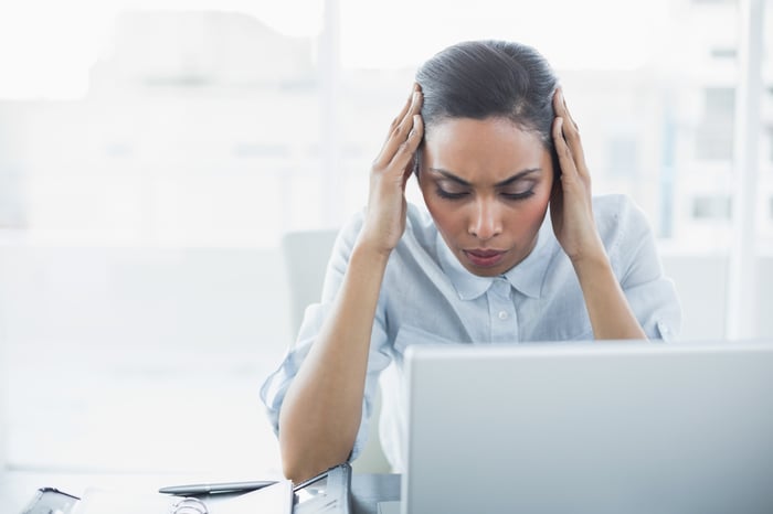 A person holding hands to the side of their head while sitting in front of a laptop.