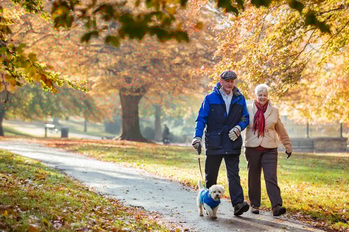 Two people walking outside with a dog on a leash.