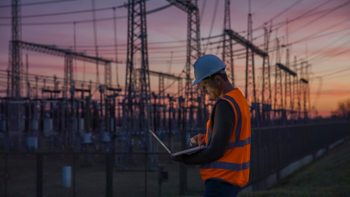 A worker stands in front of power infrastructure.