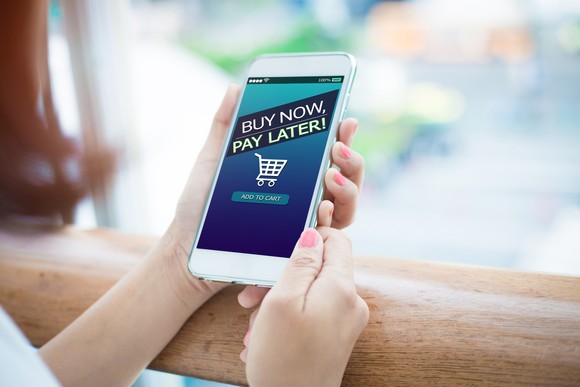 A person holding a phone with "Buy Now, Pay Later!" displayed on the screen.