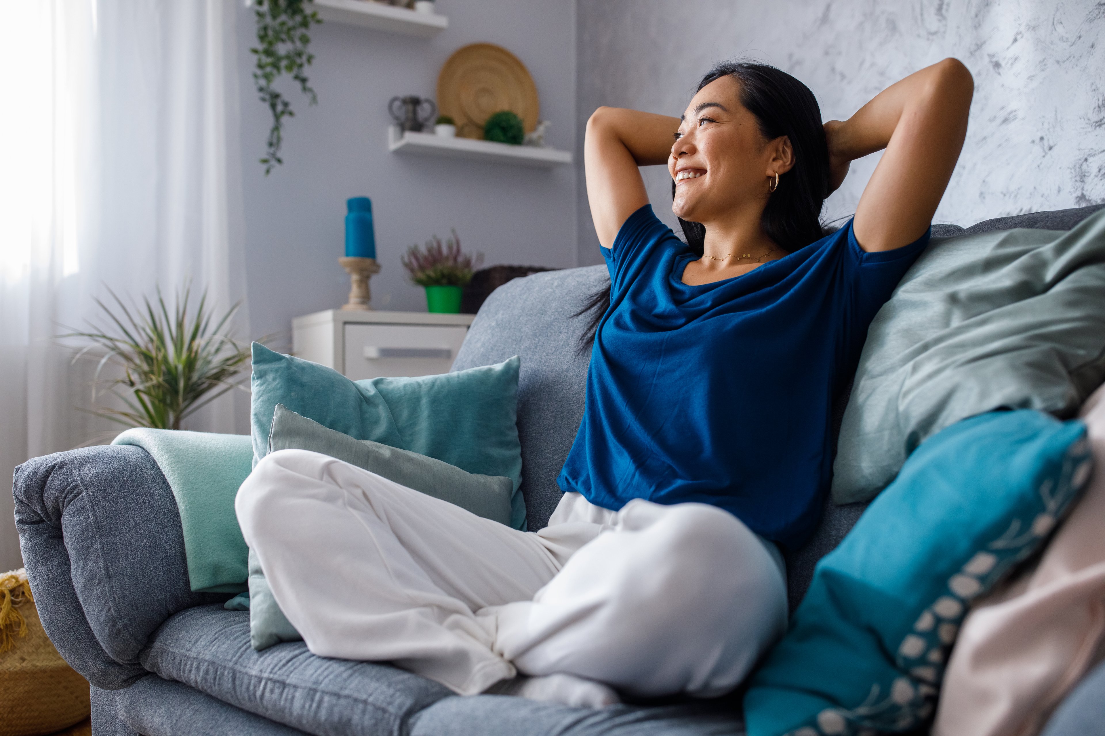 A smiling person sitting on a sofa with hands behind head.