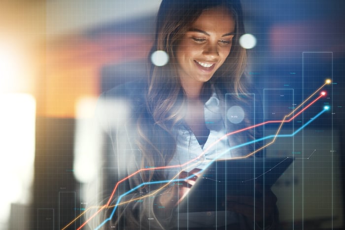 A smiling investor with a laptop and rising trend lines on a virtual stock chart. 