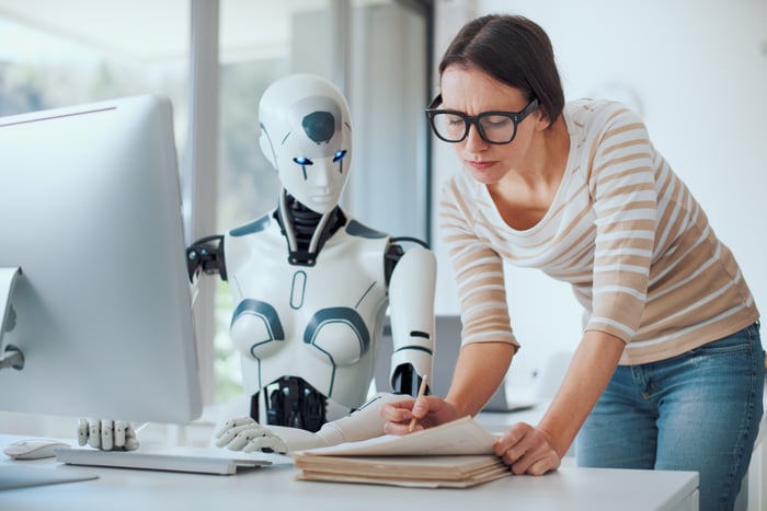 A human working with a humanoid robot at a desk.
